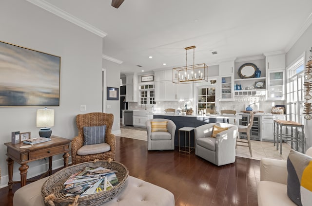 living room with crown molding, sink, wood-type flooring, an inviting chandelier, and wine cooler