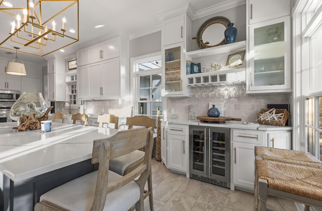 interior space featuring wine cooler, stainless steel appliances, crown molding, white cabinetry, and hanging light fixtures