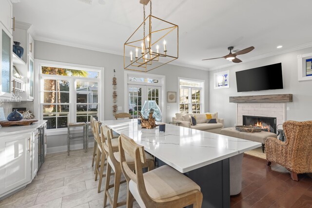 kitchen with a breakfast bar, ceiling fan with notable chandelier, ornamental molding, decorative light fixtures, and white cabinetry