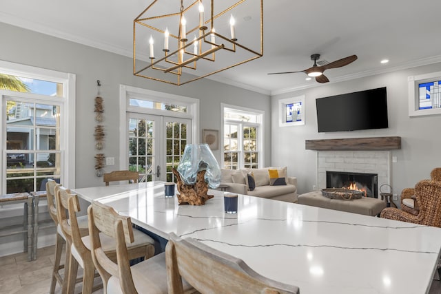 dining space with french doors, ceiling fan with notable chandelier, ornamental molding, a fireplace, and light tile patterned floors