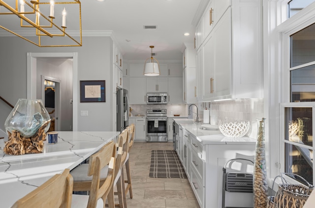 kitchen featuring white cabinets, crown molding, hanging light fixtures, light stone counters, and stainless steel appliances