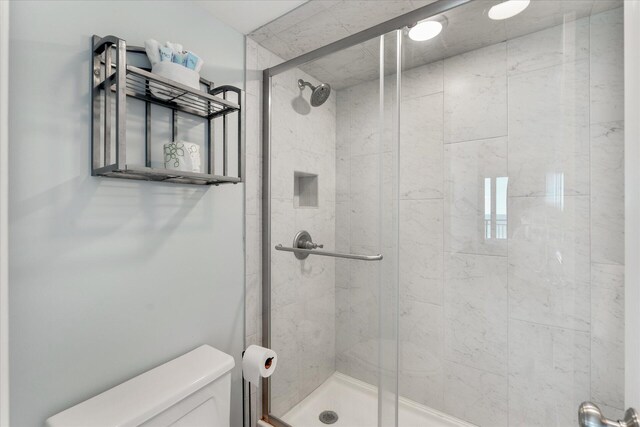 bathroom featuring a shower with door and toilet