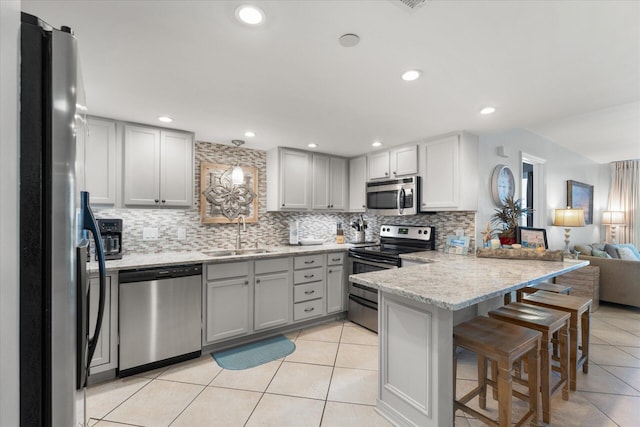 kitchen with sink, a kitchen breakfast bar, backsplash, kitchen peninsula, and appliances with stainless steel finishes