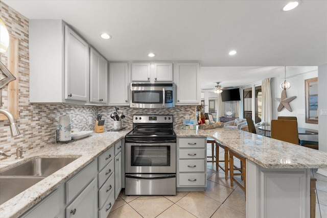 kitchen with sink, ceiling fan, light stone countertops, appliances with stainless steel finishes, and light tile patterned flooring