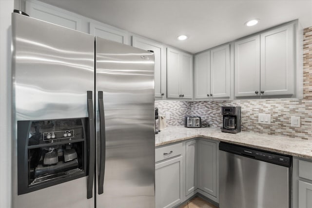 kitchen featuring gray cabinetry, decorative backsplash, light stone counters, and stainless steel appliances