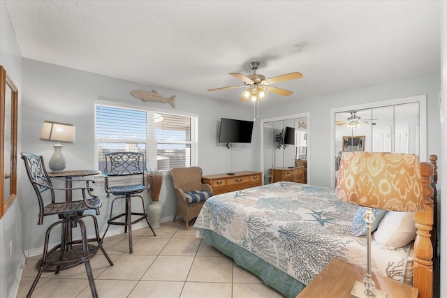 tiled bedroom featuring a textured ceiling, two closets, and ceiling fan