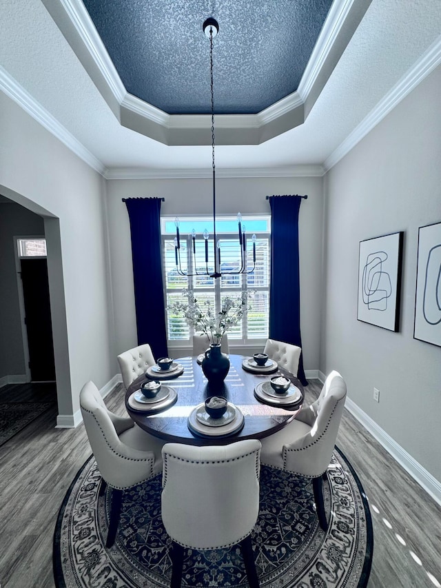 dining area featuring a raised ceiling, crown molding, a chandelier, and wood-type flooring