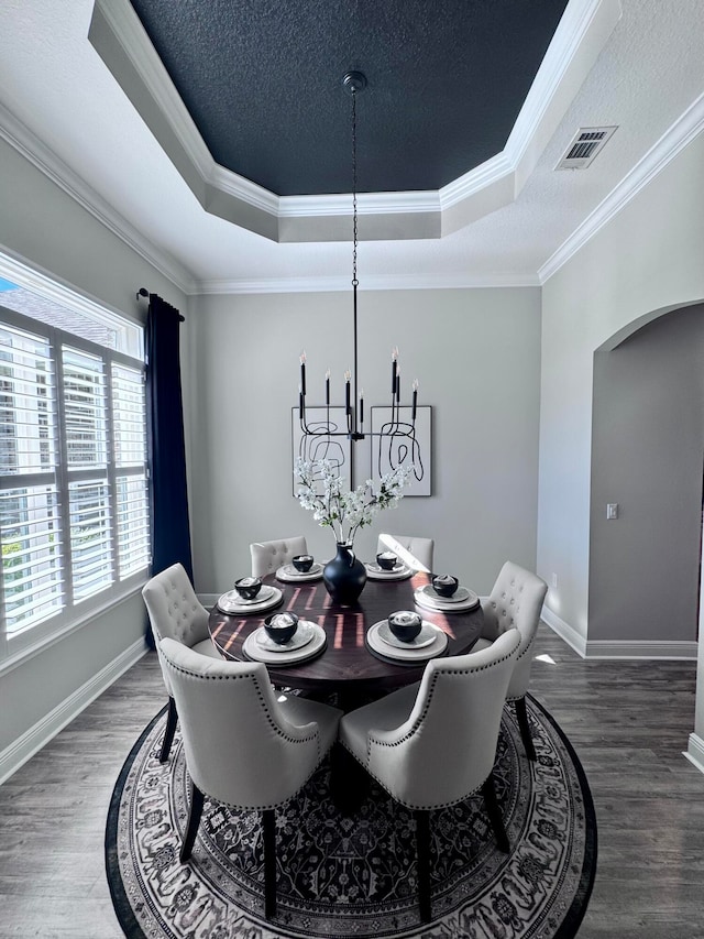 dining area with a raised ceiling, dark wood-type flooring, and crown molding