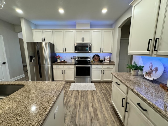 kitchen featuring white cabinets, appliances with stainless steel finishes, backsplash, and light stone counters