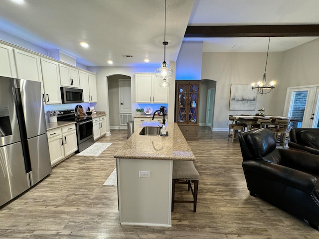 kitchen featuring sink, stainless steel appliances, beamed ceiling, an island with sink, and pendant lighting