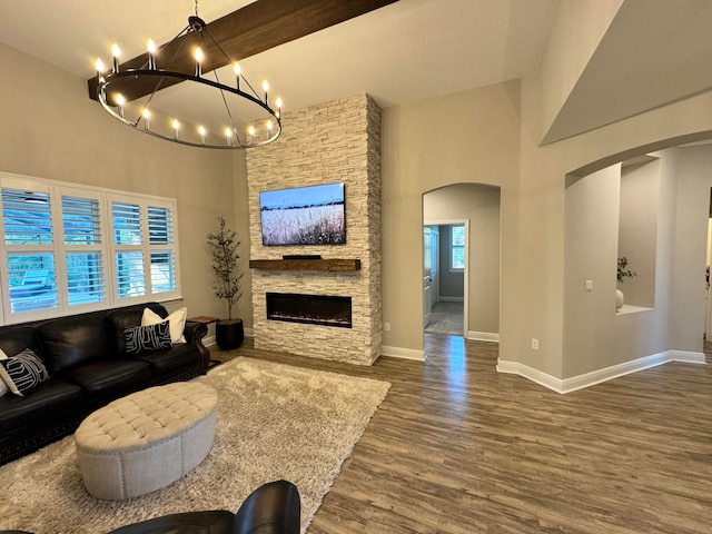 living room with a towering ceiling, a fireplace, a notable chandelier, beam ceiling, and dark hardwood / wood-style flooring