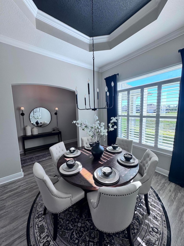 dining area with wood-type flooring, a textured ceiling, a raised ceiling, and ornamental molding