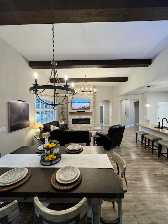 dining space featuring a chandelier, a fireplace, beamed ceiling, and wood-type flooring