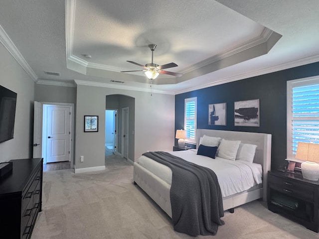 carpeted bedroom featuring a raised ceiling, ensuite bath, ceiling fan, ornamental molding, and a textured ceiling