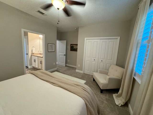 carpeted bedroom with a textured ceiling, a closet, ensuite bath, and ceiling fan