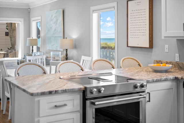 kitchen with white cabinets, high end stainless steel range, hardwood / wood-style flooring, light stone countertops, and ornamental molding