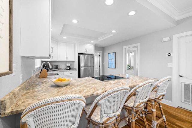 kitchen with stainless steel refrigerator, dark wood-type flooring, black electric cooktop, a breakfast bar, and white cabinets