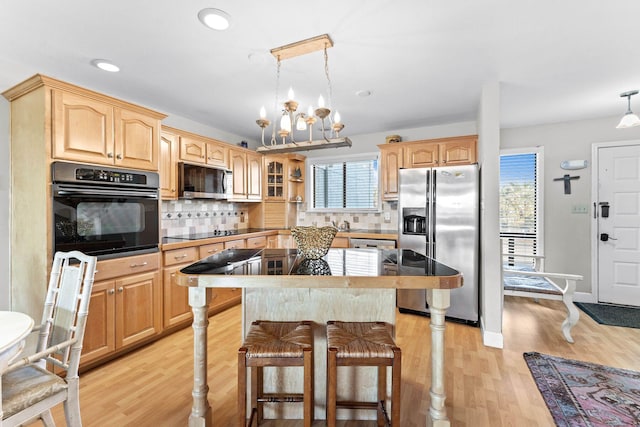 kitchen featuring decorative light fixtures, light wood-type flooring, backsplash, and black appliances