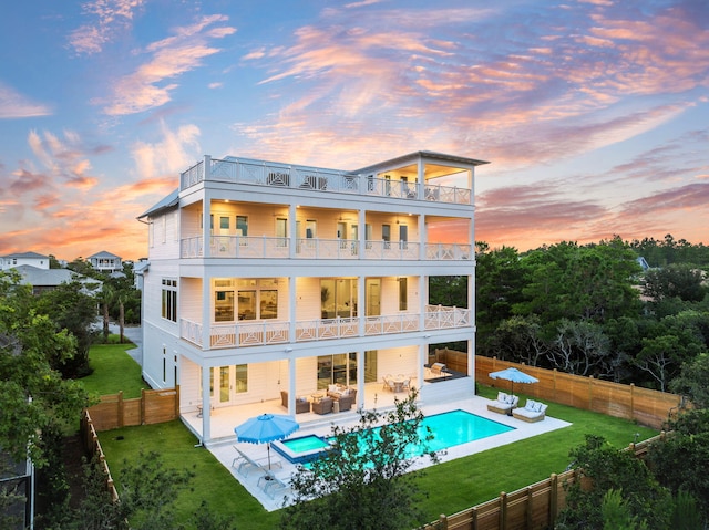 back house at dusk featuring outdoor lounge area, a fenced in pool, a balcony, a yard, and a patio