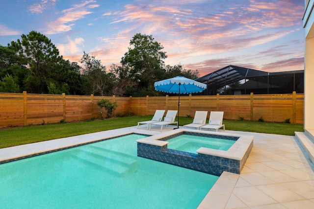 pool at dusk with an in ground hot tub, a lanai, and a lawn