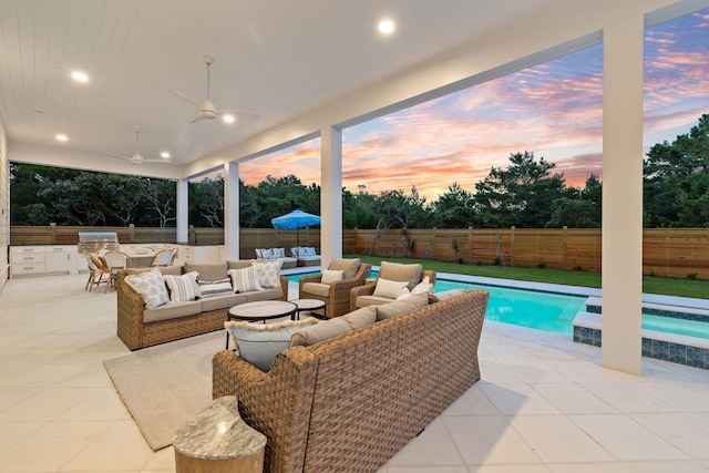 pool at dusk with ceiling fan, an outdoor kitchen, an outdoor living space, grilling area, and a patio