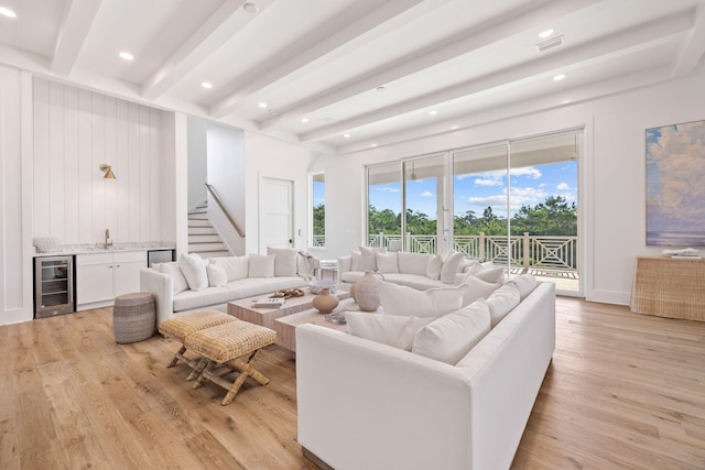 living room with beam ceiling, wet bar, beverage cooler, and light wood-type flooring