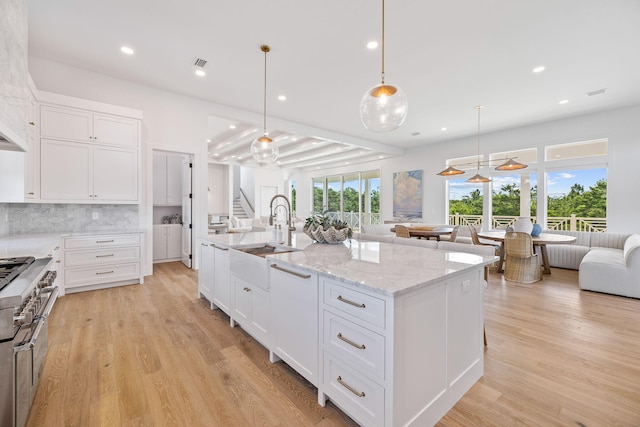 kitchen with sink, a center island with sink, light hardwood / wood-style floors, white cabinetry, and hanging light fixtures