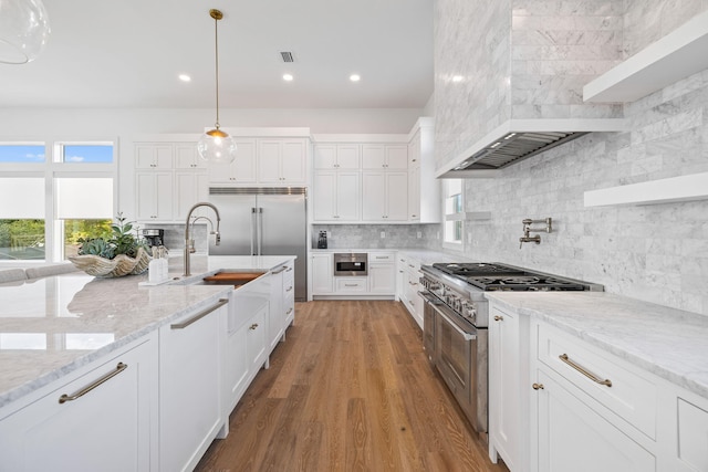 kitchen with white cabinets, light stone countertops, light wood-type flooring, tasteful backsplash, and stainless steel appliances