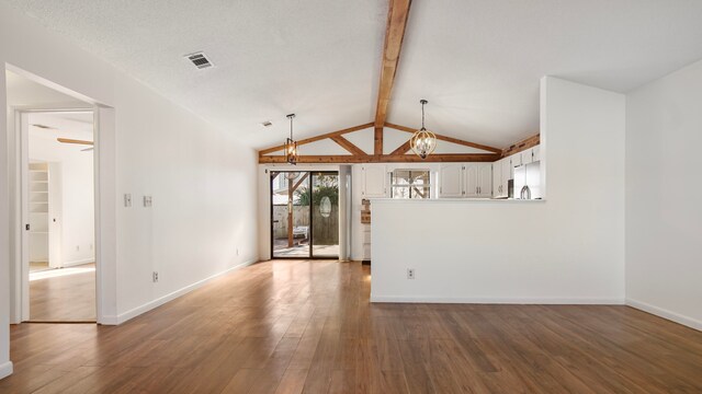 unfurnished living room featuring ceiling fan with notable chandelier, hardwood / wood-style floors, vaulted ceiling with beams, and a textured ceiling