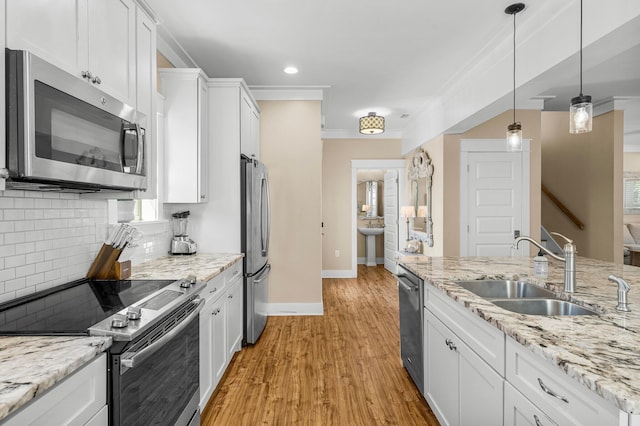 kitchen featuring appliances with stainless steel finishes, light wood-type flooring, sink, white cabinetry, and hanging light fixtures