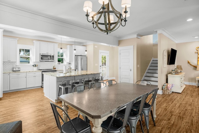 dining room with a notable chandelier, a healthy amount of sunlight, light wood-type flooring, and crown molding