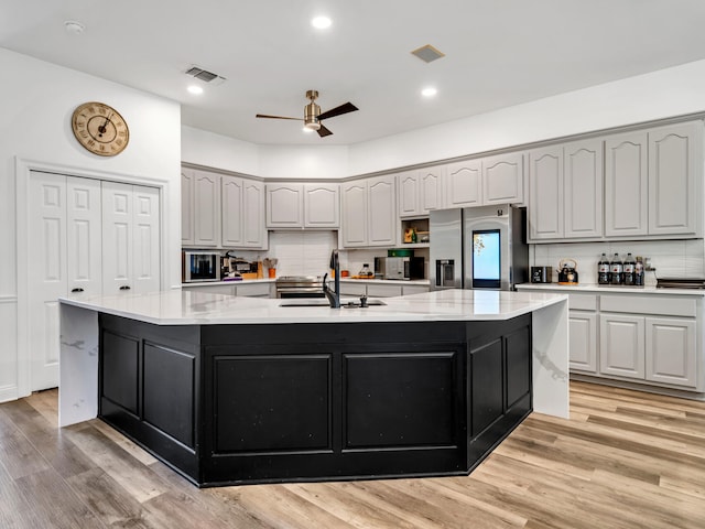 kitchen with an island with sink, light wood-type flooring, and appliances with stainless steel finishes