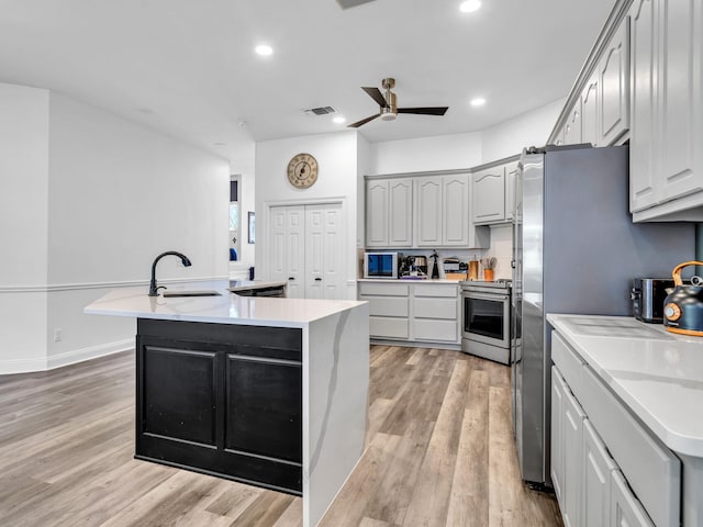 kitchen with stainless steel appliances, ceiling fan, light hardwood / wood-style floors, and an island with sink