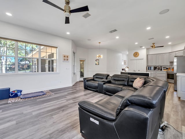 living room featuring ceiling fan with notable chandelier and light hardwood / wood-style flooring