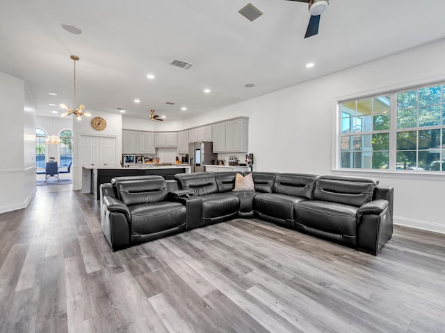 living room featuring a healthy amount of sunlight, ceiling fan with notable chandelier, and light hardwood / wood-style floors