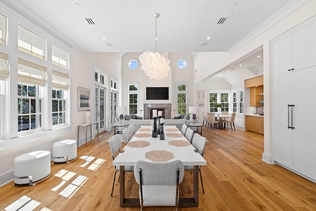 dining area with high vaulted ceiling, light hardwood / wood-style flooring, a notable chandelier, and crown molding