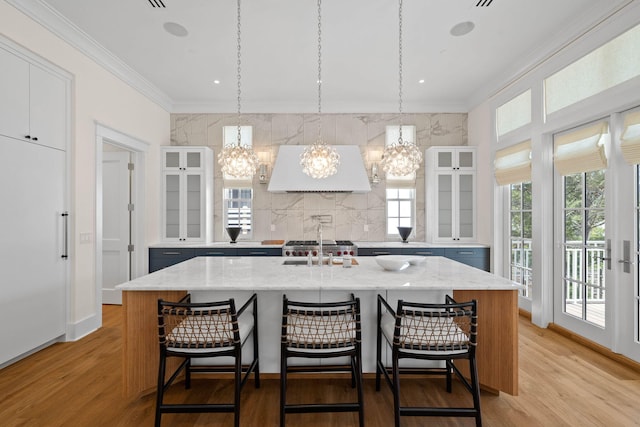 kitchen featuring built in fridge, hanging light fixtures, range hood, and an island with sink