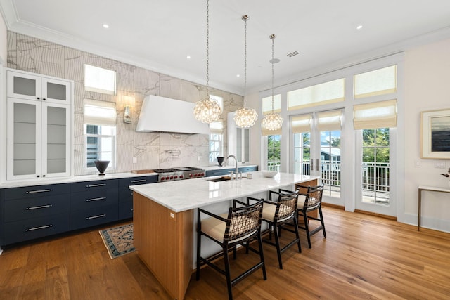 kitchen featuring a kitchen bar, custom exhaust hood, sink, decorative light fixtures, and an island with sink