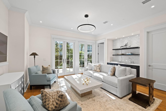 living room featuring french doors, light wood-type flooring, indoor wet bar, and crown molding