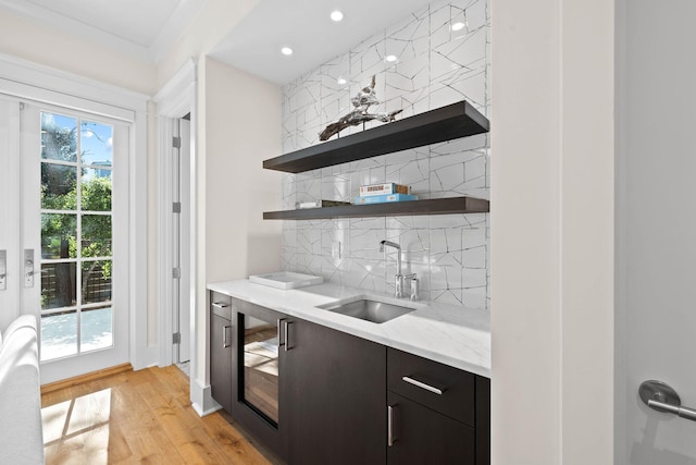 bar featuring decorative backsplash, light wood-type flooring, dark brown cabinets, sink, and wine cooler