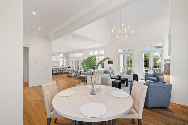 dining room featuring french doors, a high ceiling, an inviting chandelier, crown molding, and light wood-type flooring