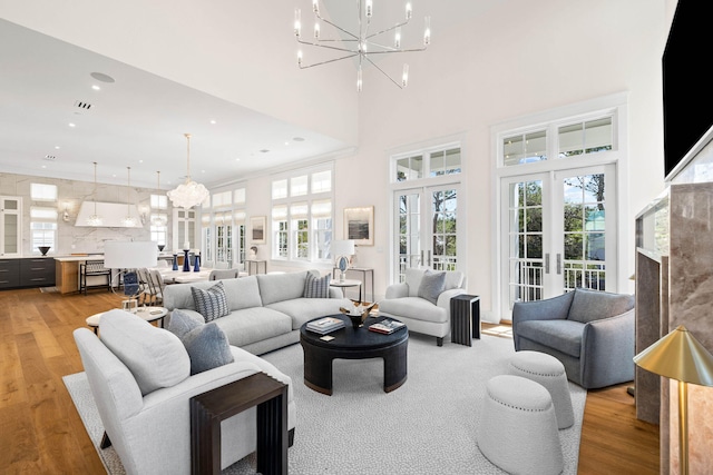 living room with light hardwood / wood-style floors, an inviting chandelier, a towering ceiling, and french doors