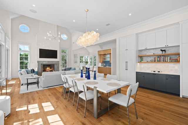 dining room featuring a notable chandelier, light wood-type flooring, crown molding, and a towering ceiling