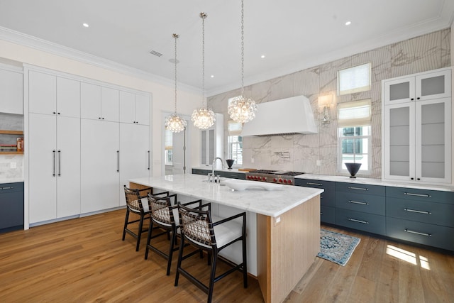 kitchen with a center island with sink, white cabinets, light wood-type flooring, and premium range hood