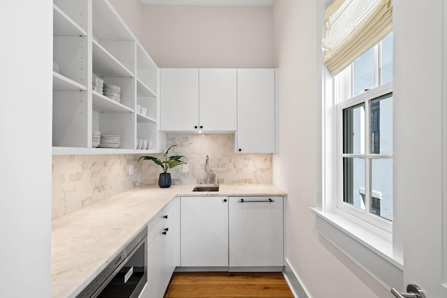 kitchen featuring white cabinetry, light stone countertops, sink, light hardwood / wood-style flooring, and decorative backsplash