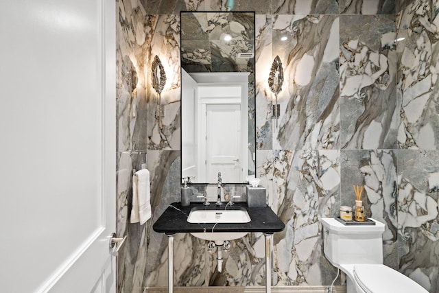 bathroom featuring toilet, tile walls, and sink