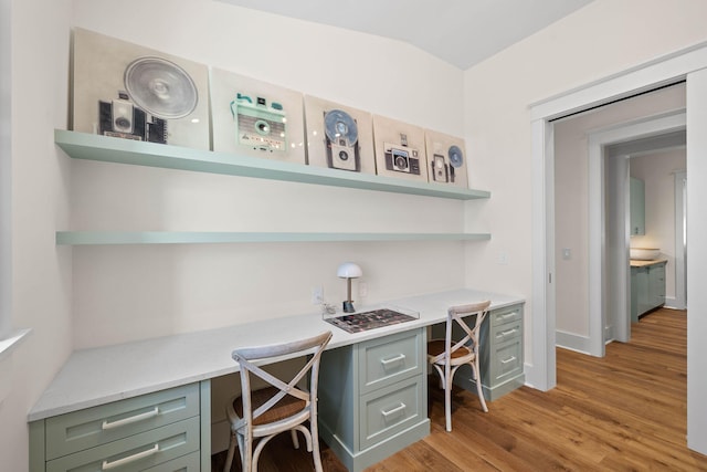 home office featuring built in desk, light hardwood / wood-style floors, and lofted ceiling