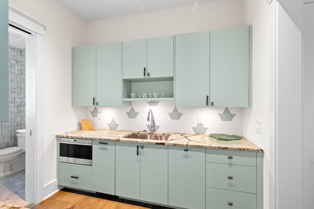 kitchen featuring backsplash, stainless steel oven, sink, light hardwood / wood-style flooring, and green cabinetry