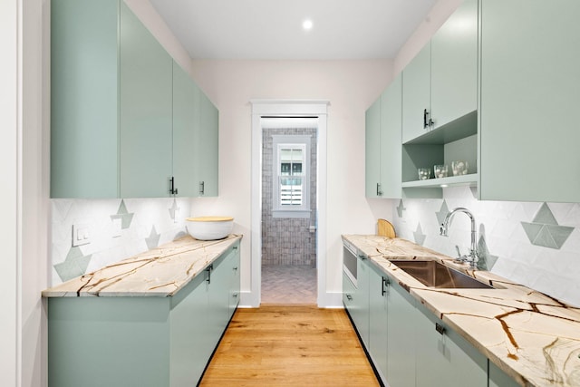 kitchen featuring decorative backsplash, light stone counters, light wood-type flooring, and sink