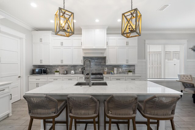 kitchen featuring a kitchen bar, light stone counters, stainless steel appliances, a kitchen island with sink, and decorative light fixtures